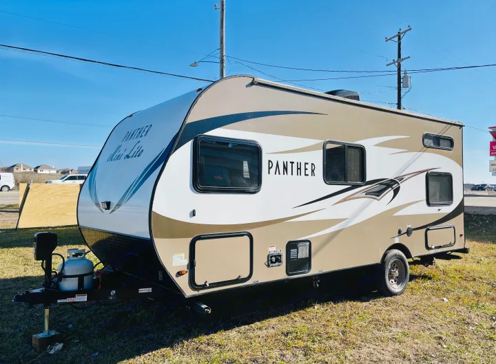 A two-tone (tan/white) Panther Mini-Lite travel trailer, an ideal RV rental for outdoor adventures. Features a propane tank.. Pacific Coachworks Panther 2019