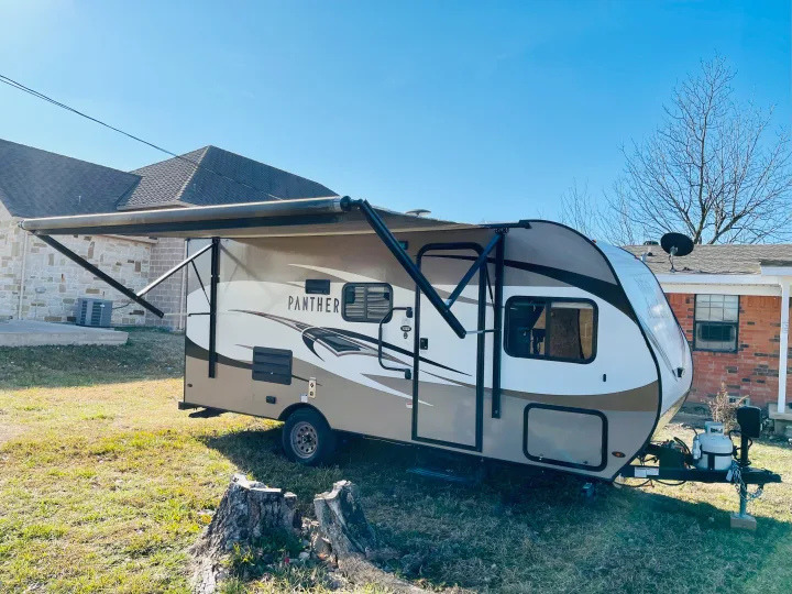 A modern Panther travel trailer with an extended awning parked on green grass. Perfect for an RV rental adventure.. Pacific Coachworks Panther 2019
