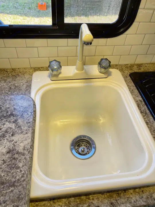 Bright RV rental kitchen with a clean sink, faucet, speckled countertop, and tiled backsplash under a window.. Pacific Coachworks Panther 2019