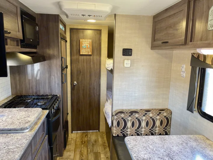 View inside an rv rental, showcasing a kitchen with stove/microwave, dinette seating, and bunk beds.. Pacific Coachworks Panther 2019