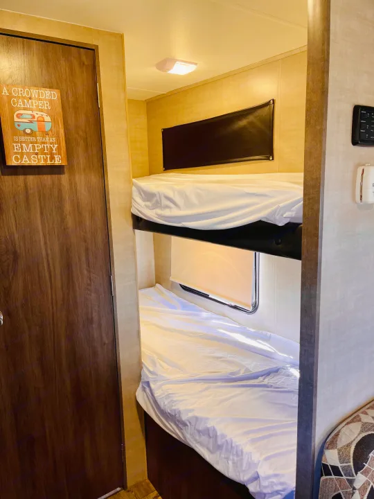 RV rental bunk beds in a cozy interior, with a fun camper sign on the door. Ready for adventure!. Pacific Coachworks Panther 2019