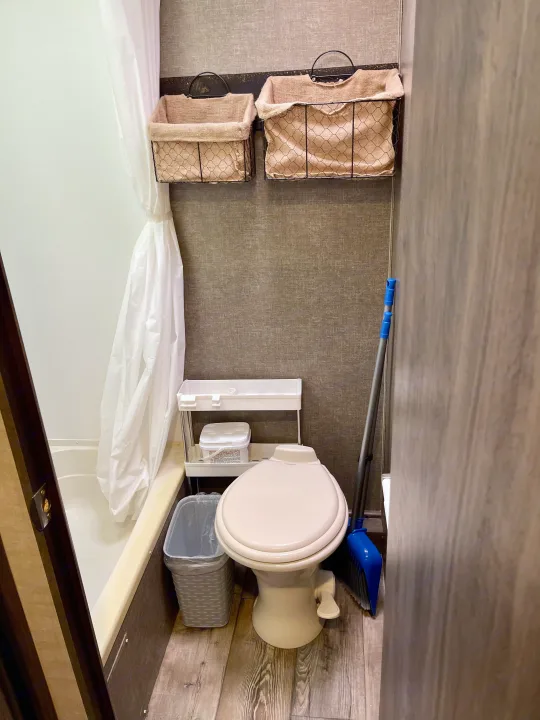 Organized RV rental bathroom: compact toilet, shower, wall baskets, and cleaning essentials for a tidy space.. Pacific Coachworks Panther 2019