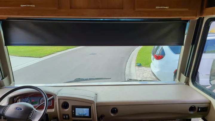 Inside an RV rental, a view from the dashboard shows the windshield, partially lowered sunshade, and a street outside.. Fleetwood Flair 2017