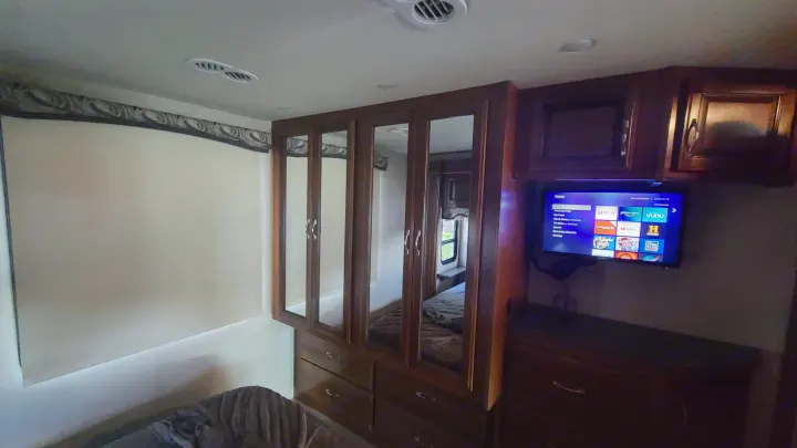 Inside an RV rental bedroom: a mounted TV displaying Roku, built-in mirrored wardrobe, and a cozy bed for rest.. Fleetwood Flair 2017