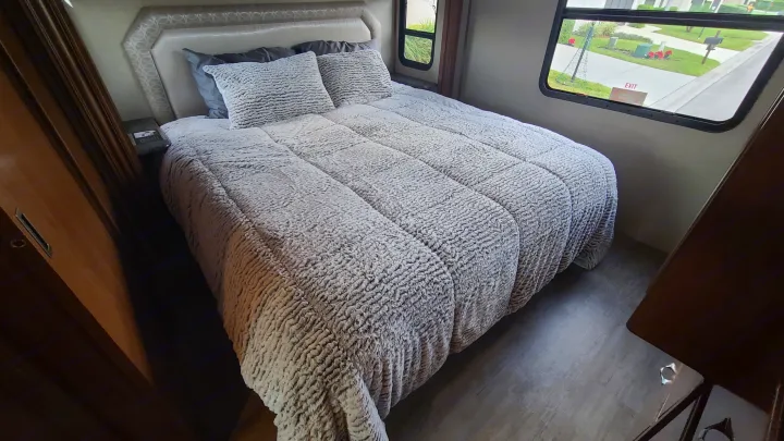 Comfortable RV rental bedroom with a soft, textured comforter, pillows, and bright windows offering a view outside.. Fleetwood Flair 2017