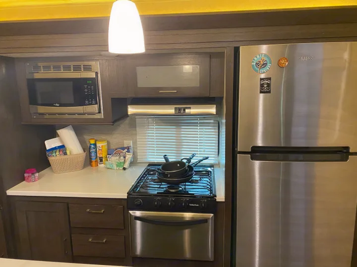 Inside an **rv rental**: a compact kitchen with microwave, Suburban stove, Whirlpool fridge, and countertop supplies.. Forest River Wildwood 2018