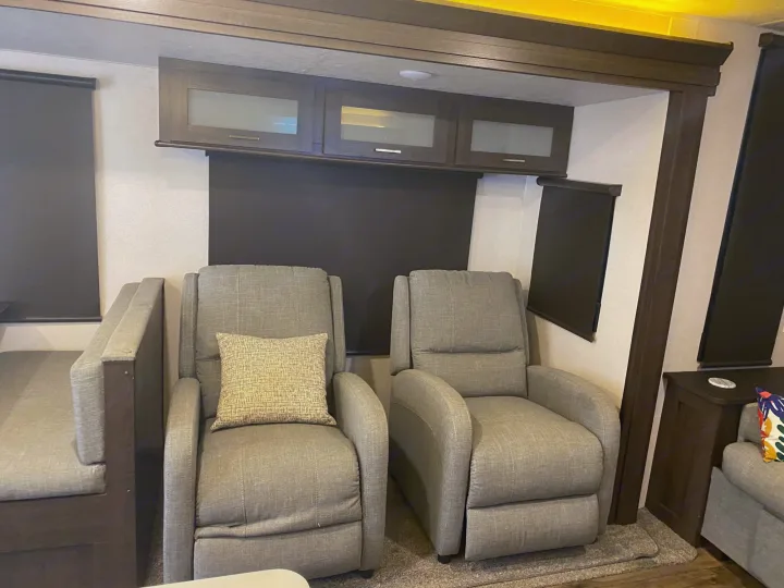 Relax in comfort! This RV rental features two grey recliners, ample overhead storage, and modern dark wood accents.. Forest River Wildwood 2018