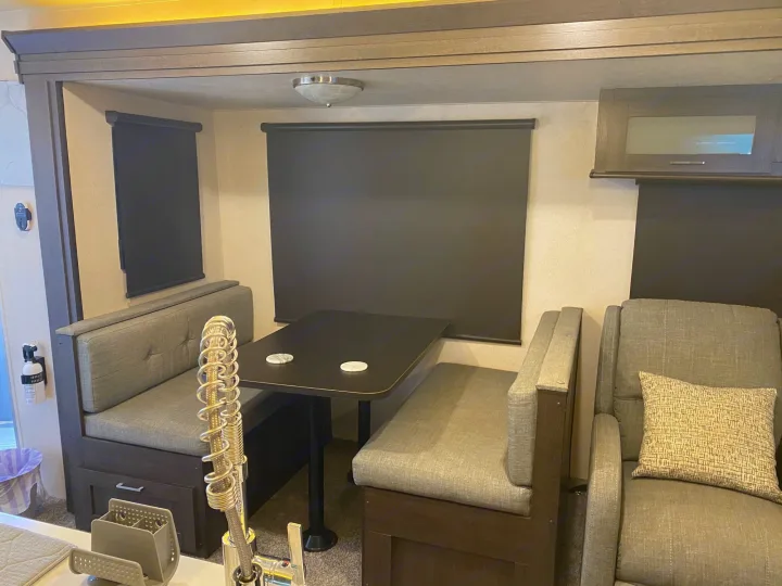 RV rental interior with a cozy dining booth, recliners, and windows covered by dark blinds, set for comfortable travel.. Forest River Wildwood 2018