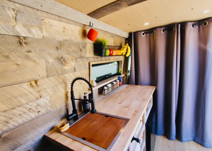 Cozy RV rental interior: wood-paneled kitchen with sink, countertop, spices, and fruit basket. Ideal for campervan living.. Mercedes-Benz Sprinter 419 LWB High Roof 2020