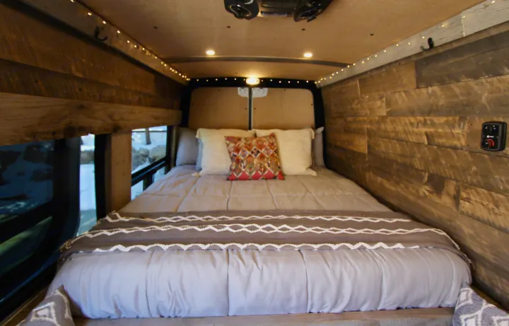 Rustic camper van bedroom for your rv rental. Features wood walls, warm string lights, comfy bedding, and a window view.. Mercedes-Benz Sprinter 419 LWB High Roof 2020