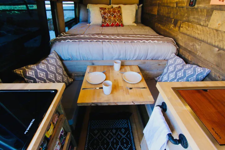 Cozy RV rental interior with a bed, dining table for two, Dometic stovetop, and Ruvati sink.. Mercedes-Benz Sprinter 419 LWB High Roof 2020