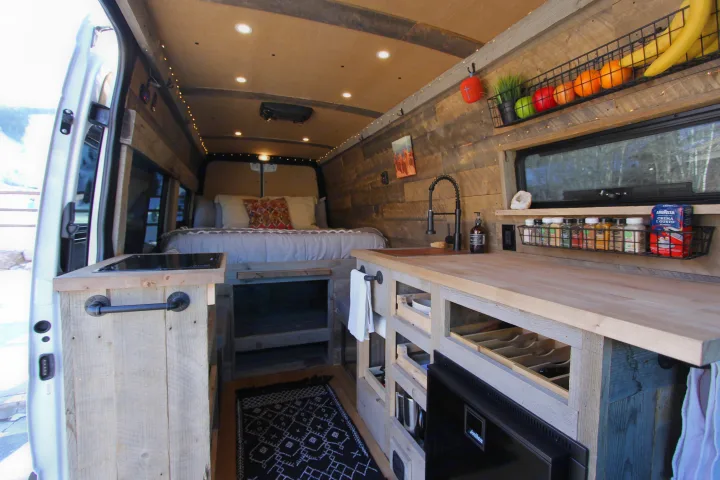 This cozy RV rental camper van interior features a kitchen, bed, and rustic wood finishes, ideal for a comfortable mobile adventure.. Mercedes-Benz Sprinter 419 LWB High Roof 2020