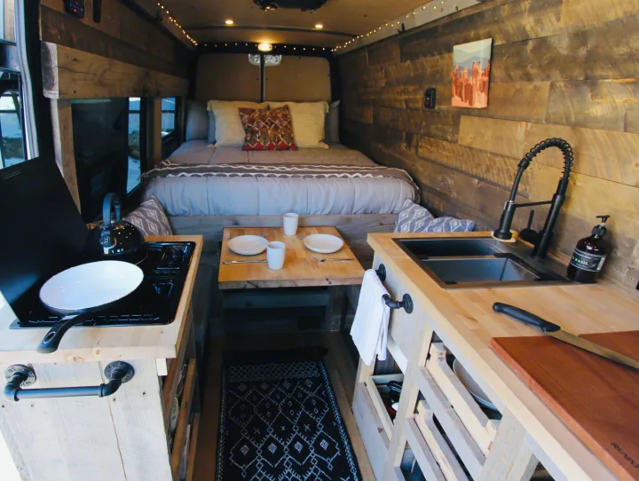 Inside an RV rental camper van: a cozy bed, compact kitchen with sink & stove, plus a dining area for comfortable travel.. Mercedes-Benz Sprinter 419 LWB High Roof 2020