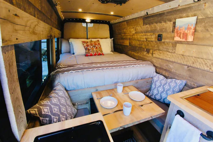 Cozy rv rental interior: a comfortable bed, rustic wooden walls, and a small dining table with place settings. Ideal camper comfort.. Mercedes-Benz Sprinter 419 LWB High Roof 2020