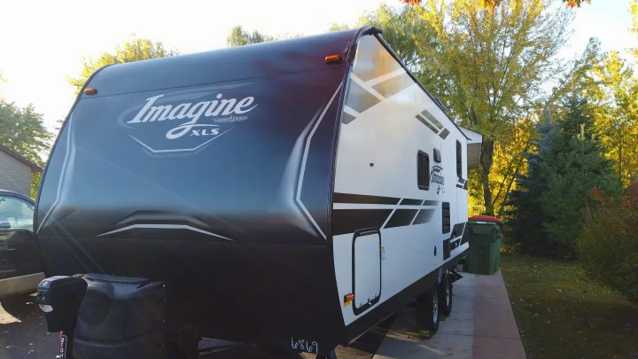 This Grand Design Imagine XLS travel trailer is ready for your next RV rental adventure, parked on a driveway with autumn trees.. Grand Design Imagine XLS 2021