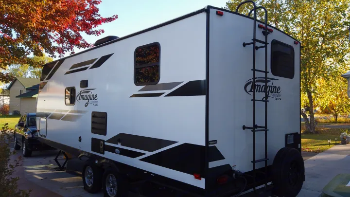 White Imagine Grand Design travel trailer, parked on a driveway with autumn trees, perfect for your next rv rental.. Grand Design Imagine XLS 2021