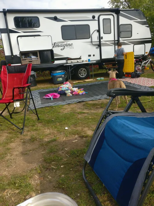 Enjoying an RV rental adventure! Family, dog, and outdoor kitchen setup at a sunny campsite with a travel trailer.. Grand Design Imagine XLS 2021