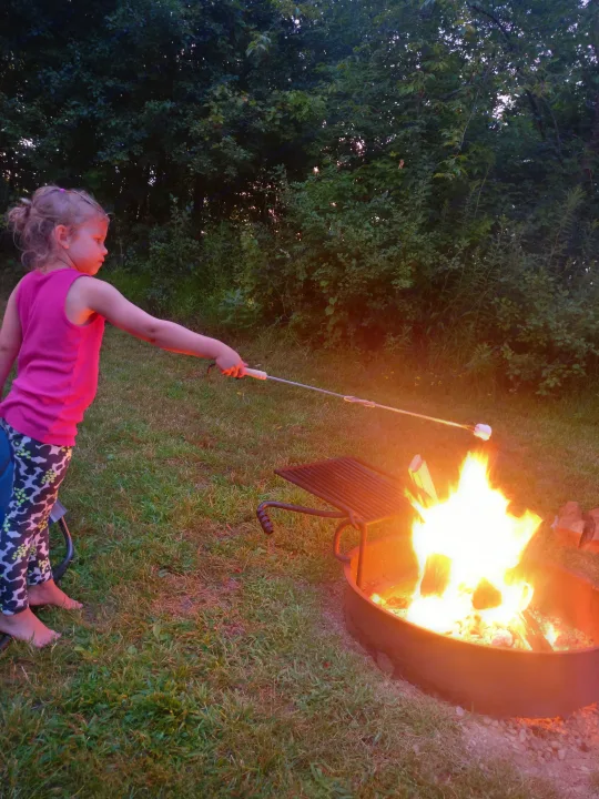 A young girl roasts a marshmallow over a vibrant campfire. An ideal outdoor experience, easily accessible with an rv rental.. Grand Design Imagine XLS 2021