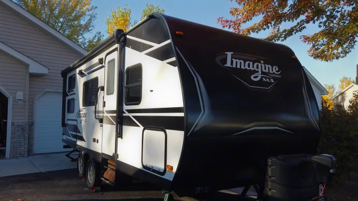 A black and white Grand Design Imagine XLS travel trailer is parked in a residential driveway, an ideal RV rental for adventures.. Grand Design Imagine XLS 2021