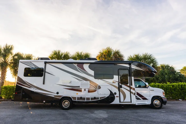 White Esteem Integra RV rental parked on asphalt, glowing in warm light with palm trees and a bright sky.. Entegra Coach Esteem 31F 2021