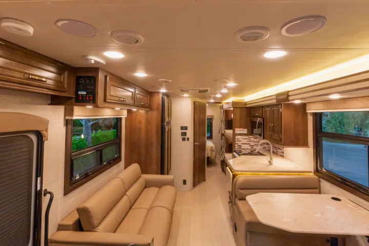 An RV rental's spacious interior features a bright kitchen, dining booth, plush sofa, and visible rear sleeping areas.. Entegra Coach Esteem 31F 2021