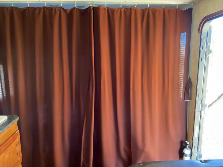 Dark brown privacy curtain inside an RV rental, separating an area. An exit door and fire extinguisher are on the right.. Gulf Stream Kingsport 2015