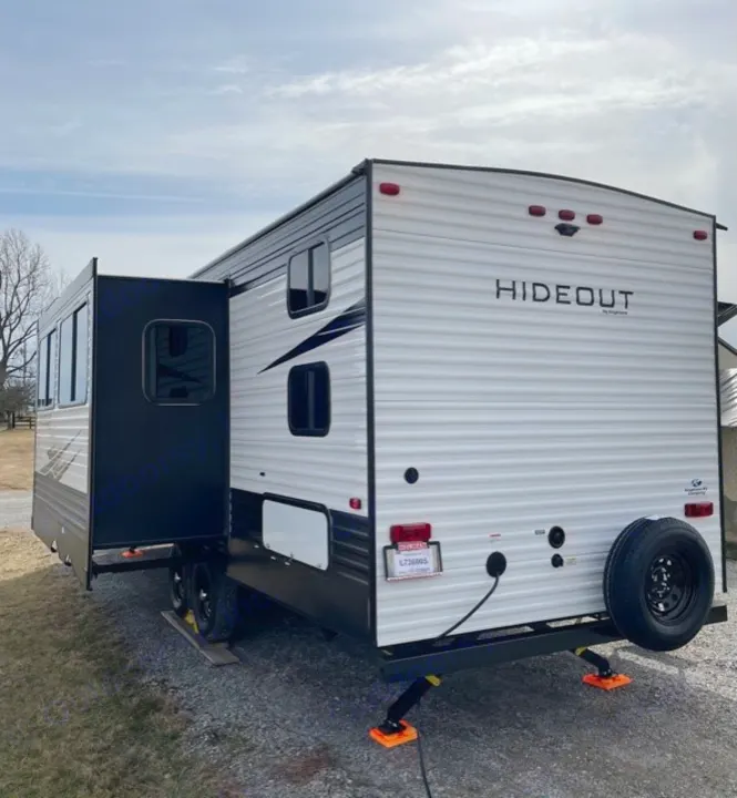 A white Hideout travel trailer rv rental with its large side slide-out extended and rear stabilizers down.. Keystone Hideout 2021