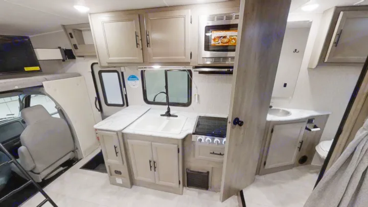 RV rental interior showcasing a compact kitchen with a sink and stove, a cozy bathroom, and an overhead bunk bed.. Coachmen Freelander 2022