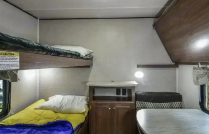 Inside an RV rental: bunk beds, a dining area with patterned seating, and a middle storage cabinet.. Heartland Prowler Lynx 2018