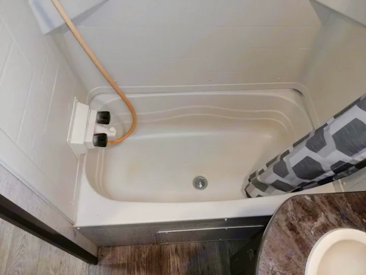 Inside an RV rental, a clean, compact shower/bathtub features a handheld showerhead and a patterned curtain.. Heartland Prowler Lynx 2018