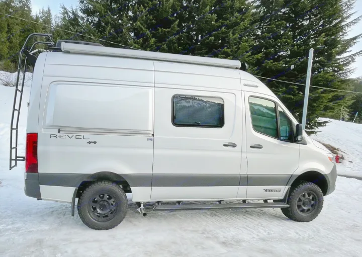 Silver Winnebago Revel 4x4 camper van, a robust rv rental for winter. Parked on snow with forest backdrop.. Winnebago Revel 2021