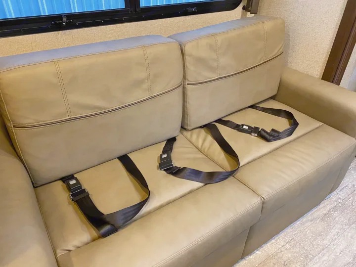 This tan RV rental sofa features black lap seatbelts, a common and essential safety feature for motorhome travel.. Thor Hurricane 2019