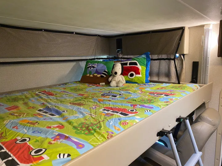 Inside an RV rental, a child's bunk bed with a patterned sheet, safety net, Snoopy, and raccoon pillow.. Thor Hurricane 2019