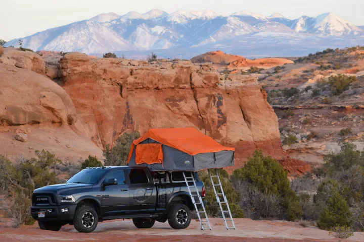 Adventure-ready Ram truck with an orange rooftop tent deployed in a rocky desert. A rugged rv rental option for overlanding & camping.. RAM Power Wagon 2018