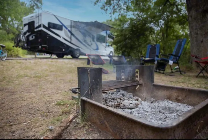 RV rental parked at a serene campsite with a fire pit, chairs, and bike. Ideal for your next outdoor adventure.. Thor Motor Coach Chateau 2021