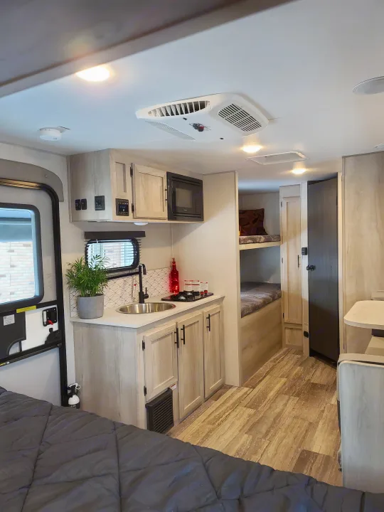Step inside this RV rental: a bright interior with light wood kitchen, sink, microwave, bunk beds, and main sleeping area.. K-Z Manufacturing Escape 191bhk 2021