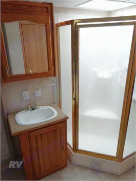 Step inside this RV rental bathroom with a functional vanity, sink, mirror, and a gold-framed corner shower.. Other Other 2005