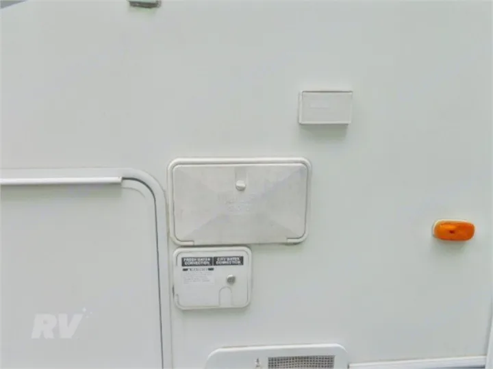 RV rental's side: outdoor shower, fresh/city water connections, utility panels, and an amber marker light.. Other Other 2005