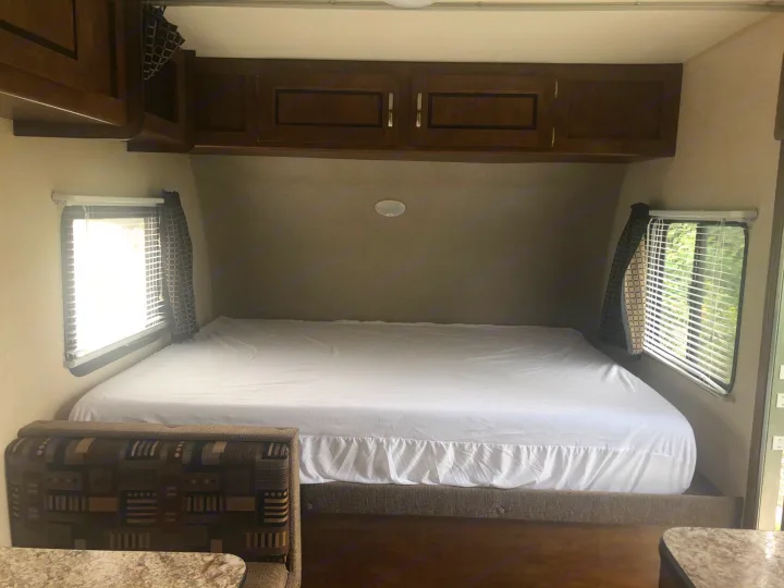 RV rental sleeping area: A neat bed with white sheets, overhead cabinets, and side windows in a cozy camper interior.. Forest River Salem Cruise Lite 2017