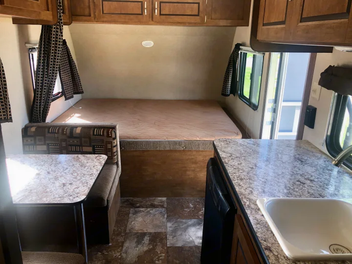 An RV rental interior, showcasing a comfy bed, a dining booth, and a practical kitchenette with a sink.. Forest River Salem Cruise Lite 2017
