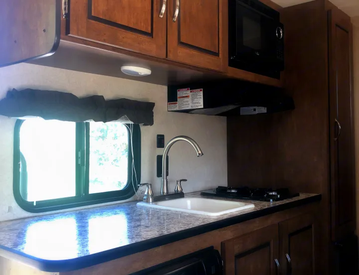 Interior of an RV rental kitchen featuring wood cabinets, a sink, stove, and microwave, offering a compact, functional space.. Forest River Salem Cruise Lite 2017