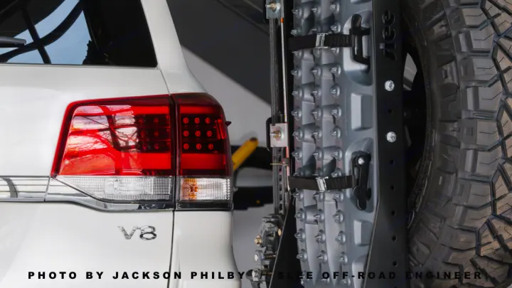 Rear view of a white V8 SUV with red taillights, off-road recovery boards, and a spare tire, ideal for adventure trips complementing an RV rental.. Toyota Land Cruiser 200 Series 2021