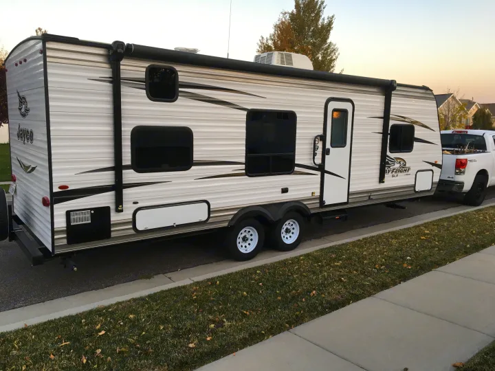Jayco travel trailer RV rental attached to a white pickup truck, parked on a suburban street. Ready for your next journey!. Jayco Jay Flight 2018