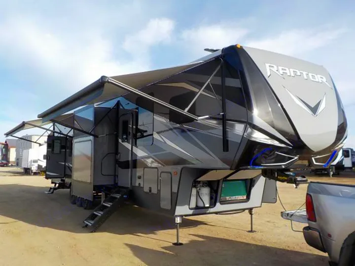 A large, gray & black Raptor fifth-wheel toy hauler RV, fully set up with awnings out, ready for an rv rental adventure.. Keystone Raptor 2020