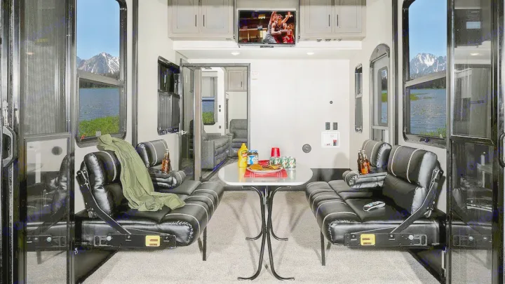 Inside this RV rental: versatile living/dining space with a TV, comfy seating, and stunning mountain lake views. Ideal for trips!. Keystone Raptor 2020