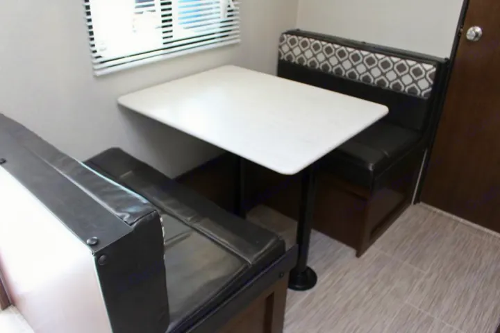 This cozy RV rental features a dinette with black benches, a bright white table, and blinds on the window.. Prime Time NAVI 2019