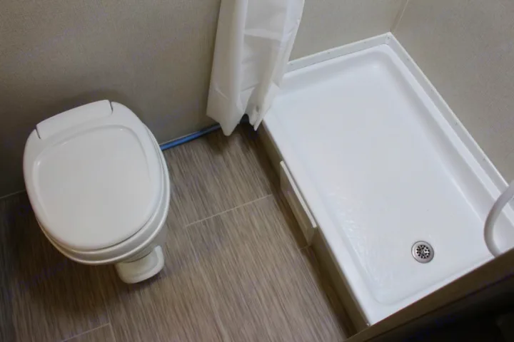 Compact RV rental bathroom features a white toilet on the left and a shower pan with drain on the right.. Prime Time NAVI 2019