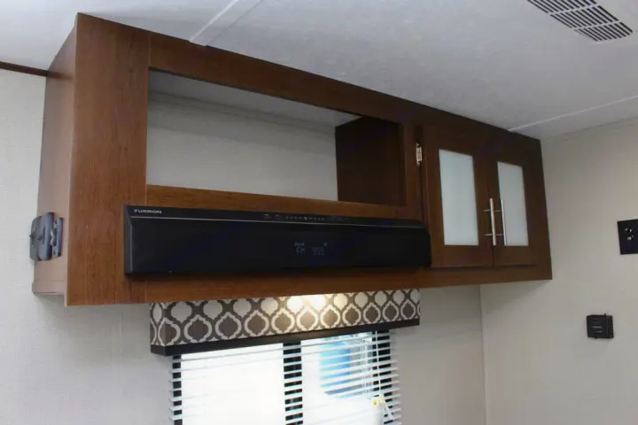 RV rental interior showcasing overhead cabinets, Furrion stereo, and a window with patterned valance.. Prime Time NAVI 2019