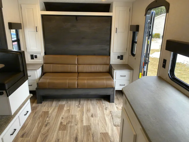 RV rental interior: cozy living space with a brown convertible sofa bed, white cabinets, and wood-style floor.. Keystone Hideout 2021