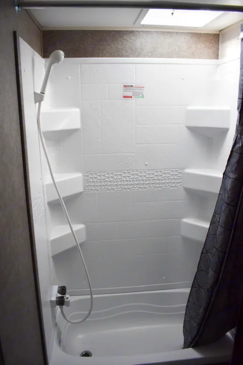 RV rental shower interior with white walls, handheld showerhead, built-in shelves, and small tub.. Open Range 20MB 2021